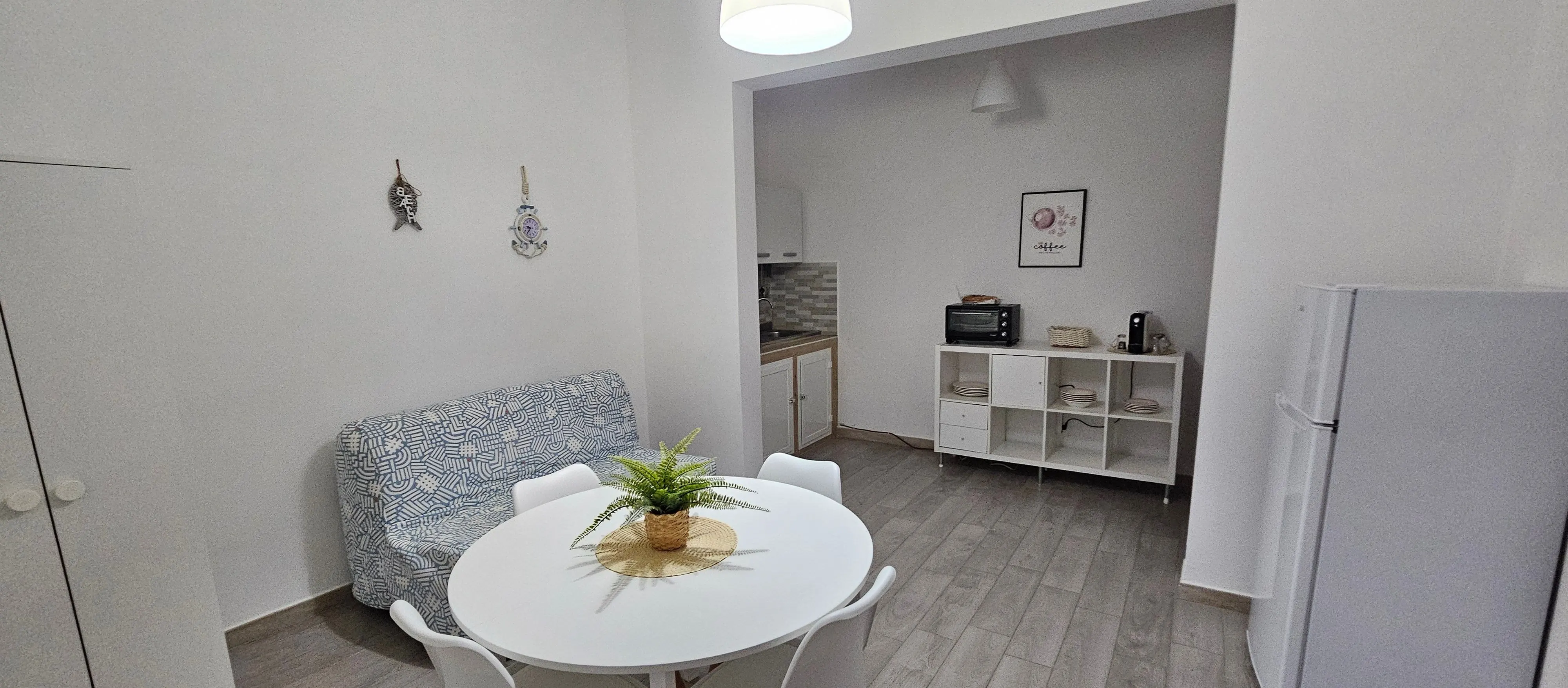 Zona pranzo dell'appartamento con divano letto, tavolo tondo e angolo cottura sullo sfondo.