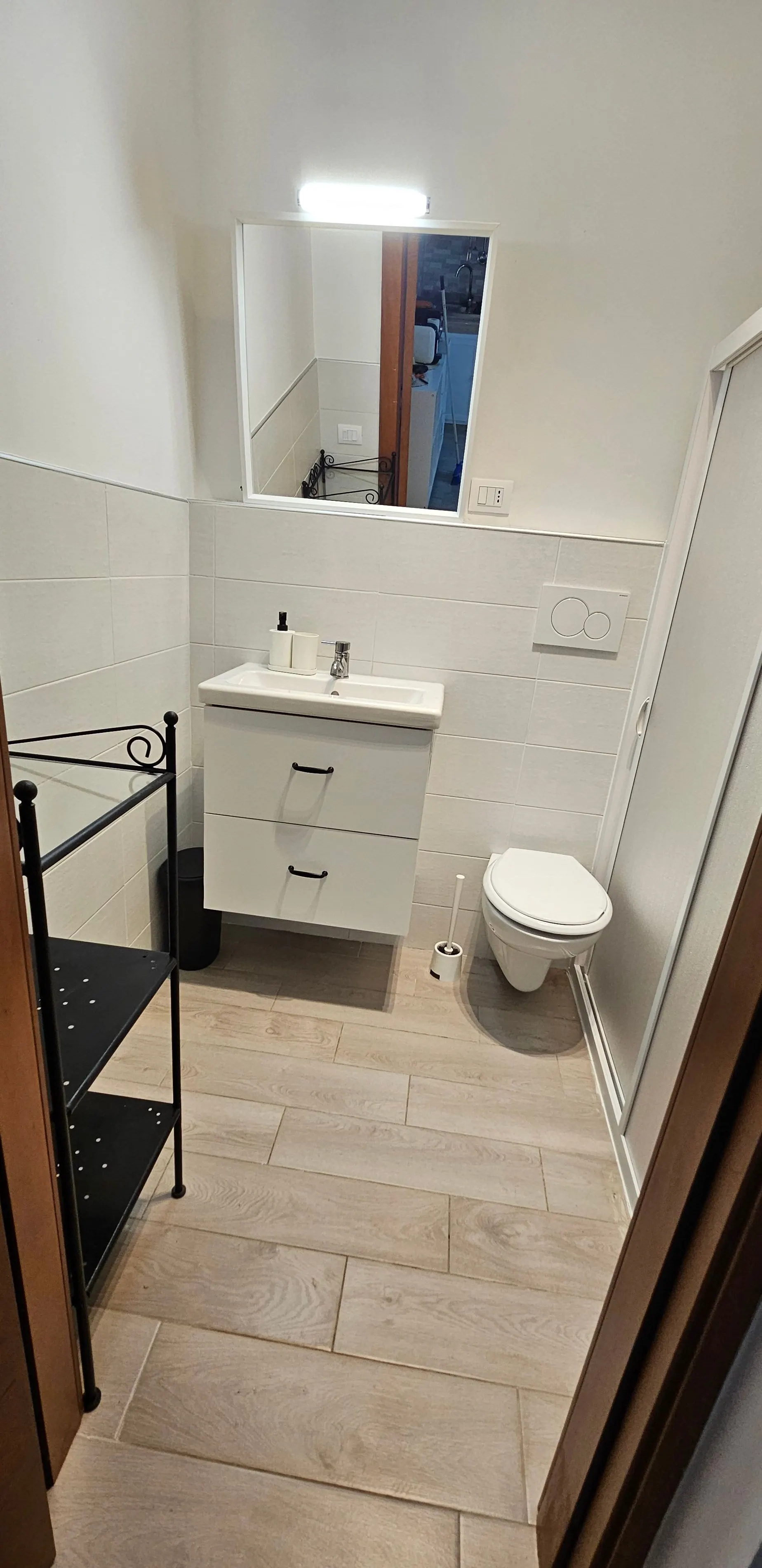 Bagno con lavabo, mensola, sanitari e pavimento piastrellato a effetto legno chiaro.