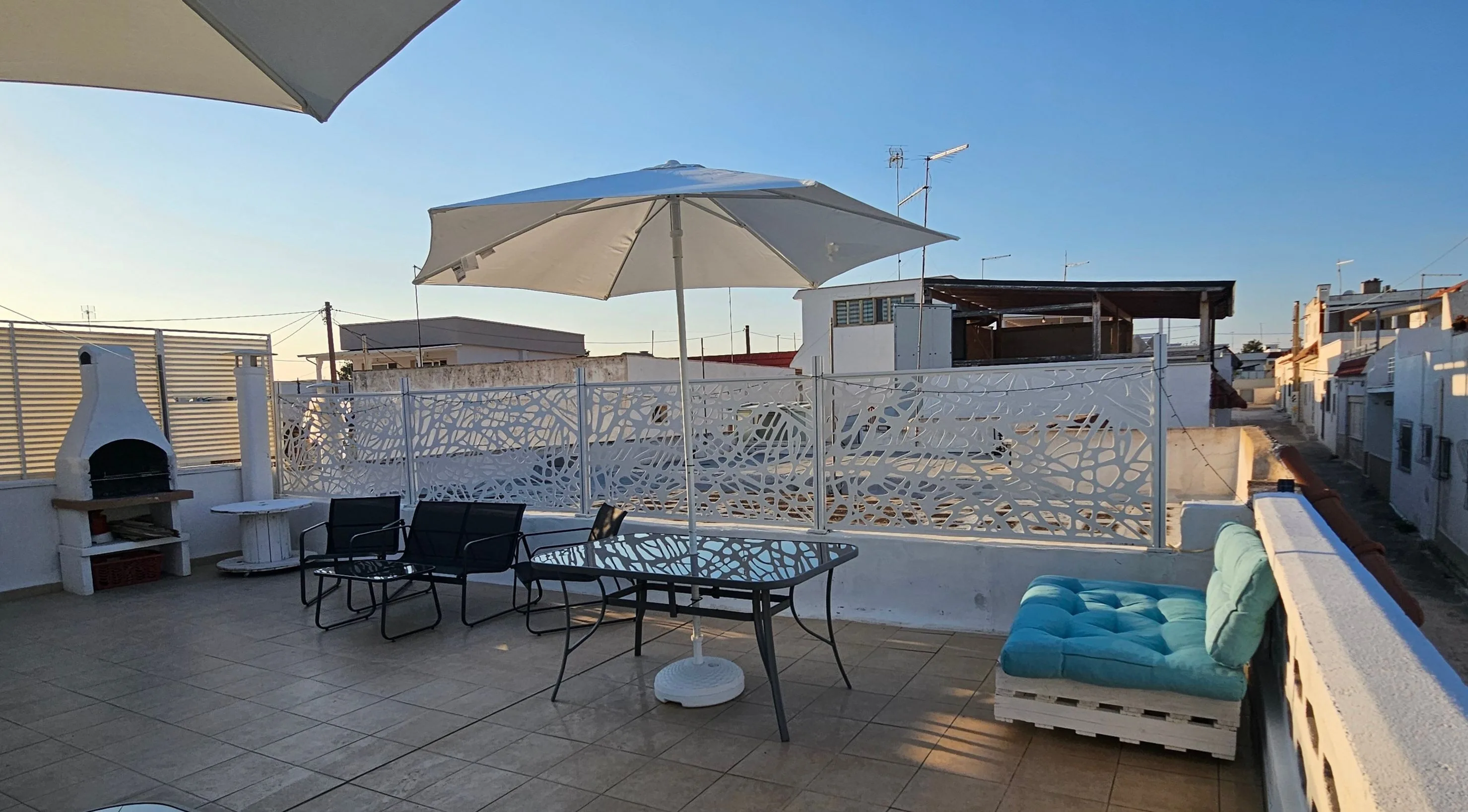 Terrazza con barbecue in muratura, tavolo con ombrellone e pallet sofa con cuscini azzurri.